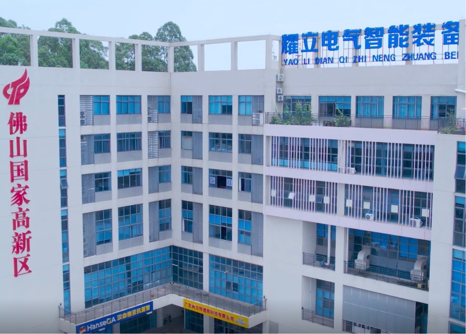 现代化工业厂房外景，灰色建筑配蓝色玻璃幕墙，绿色植物环绕，阳光明媚天气